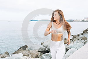 Young fit beautiful woman with long hair in white sport clothes running and enjoy life on sea beach