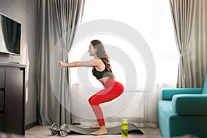 Young fit beautiful woman in sportwear doing everyday warm up home exercises with dumbbell on the mat in living room, sportive