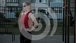 young fit blond busty woman with ponytail in red top exhales at sports ground