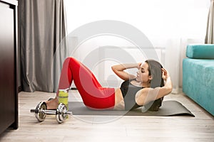 Young fit brunette woman in sportwear doing abdominals with crunch on the mat in living room during home workout, sportive