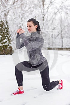 Young fit caucasian woman doing lunge exercise in snow at winter