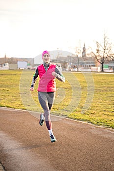 Young fit caucasian woman in fitness clothes running on track in park on sunrise