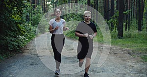 Young fit couple atheltes running on running road in a forest.