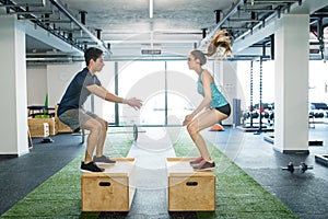 Young fit couple exercising in gym, doing box jumps.