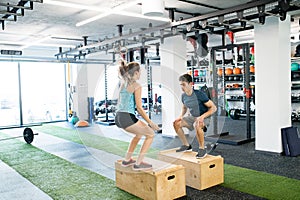 Young fit couple exercising in gym, doing box jumps.