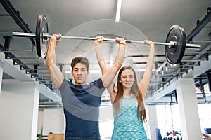 Young fit couple in gym lifting heavy barbell.