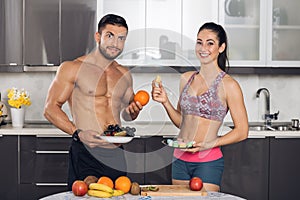 Young fit couple in kitchen with fruits and macarons