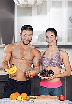 Young fit couple in the kitchen, holding fruits