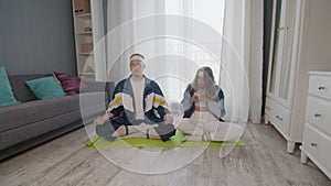 Young fit family sitting on the floor, meditating together, keeping a healthy lifestyle. Woman take photo on her
