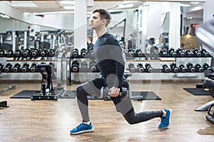 Young fit handsome man doing exercises with weights in gym.