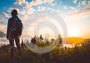 Young fit happy woman stand on viewpoint after reach top in mountains. Carefree tourist woman looking at sun enjoying landscape.