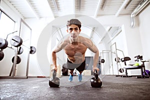 Young fit hispanic man in gym doing push ups on kettlebells