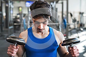 Young fit hispanic man in gym exercising with dumbbells.