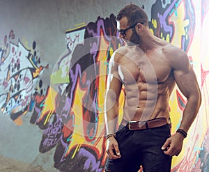 Young fit macho man posing in front of graffiti wall