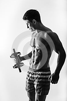 Young and fit male model posing his muscles pumping up with dumbbells in a gym looking to the left isolated on white