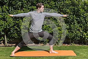 Young fit male practicing yoga and doing the warrior pose outdoors