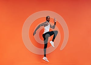 Young fit man doing exercises in studio. Male athlete jumping in the air over an orange background