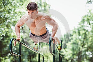 Young fit man doing push ups on bars