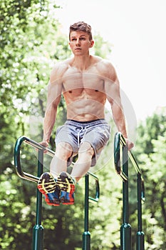 Young fit man doing push ups on bars