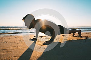 Young fit man doing push ups or exercising on the beach during sunrise