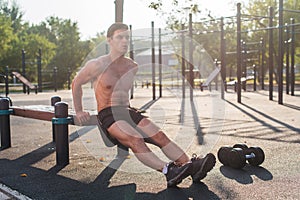 Young fit man doing triceps dips exercises during outdoor cross training workout. Fitness male model.