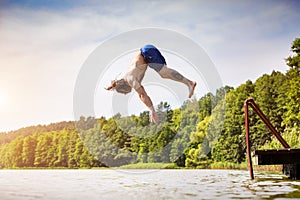 Young fit man jumping into a lake