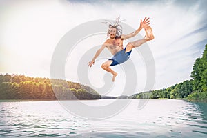 Young fit man making a jump into a lake.