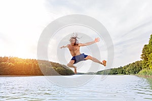 Young fit man making a jump into a lake.