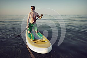 Young fit man on paddle board floating on lake.