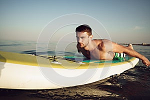 Young fit man on paddle board floating on lake.