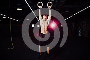 Young fit man pulling up on gymnastic rings.