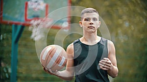 A young fit man standing on a sports ground and holding a basketball ball