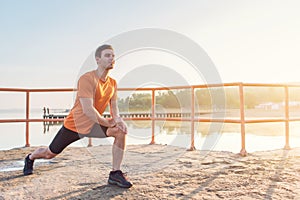Young fit man stretching legs outdoors doing forward lunge.
