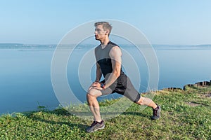 Young fit man stretching legs outdoors doing forward lunge.