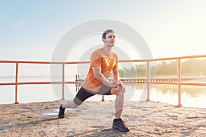 Young fit man stretching legs outdoors doing forward lunge.