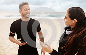 Young fit man and woman couple wearing sportswear, using smartphones by seaside, preparing for training