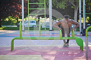 Young fit shirtless black man doing push-ups on parallel bars.