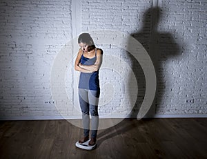 Young fit and slim woman checking body weight on scale with big edgy shadow light sad and desperate