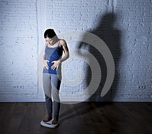 Young fit and slim woman checking body weight on scale with big edgy shadow light sad and desperate