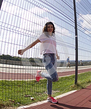 Young fit sports lady.She is posing on a fence off the basketball court.