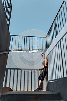 Young, fit and sporty brunette girl in sportswear. A tired athlete leaned against a concrete wall.