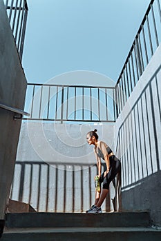 Young, fit and sporty brunette girl in sportswear. A tired athlete leaned against a concrete wall.