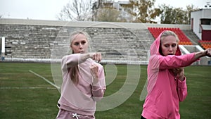 Young fit sporty caucasian pretty twin sisters boxing outdoors at stadium field