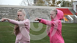 Young fit sporty caucasian pretty twin sisters boxing outdoors at stadium field