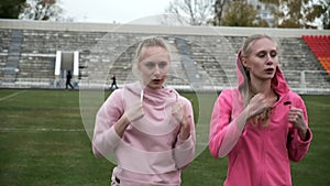 young fit sporty caucasian pretty twin sisters boxing outdoors at stadium field