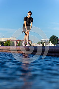 Young, fit and sporty girl in black clothes stretching after the workout near the public fountain in the urban city park