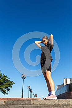 Young, fit and sporty girl in black clothes stretching after the workout in the urban city park