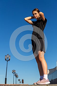 Young, fit and sporty girl in black clothes stretching after the workout in the urban city park