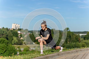 Young, fit and sporty girl in black clothes stretching after the workout in the urban city park