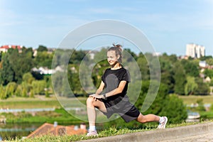 Young, fit and sporty girl in black clothes stretching after the workout in the urban city park